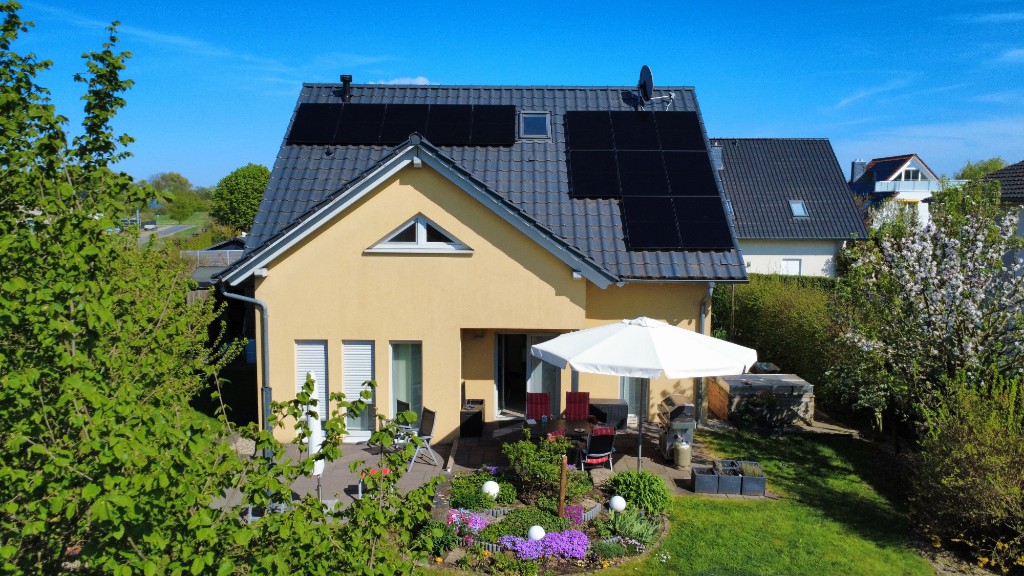 Photovoltaik Referenz – gelbes Einfamilienhaus mit Solarmodulen, Gartenansicht
