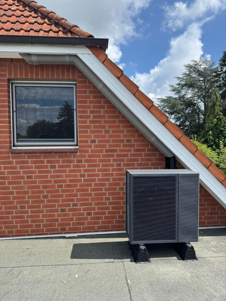Wärmepumpe Referenz – Panasonic Außengerät auf Flachdach vor Ziegelwand